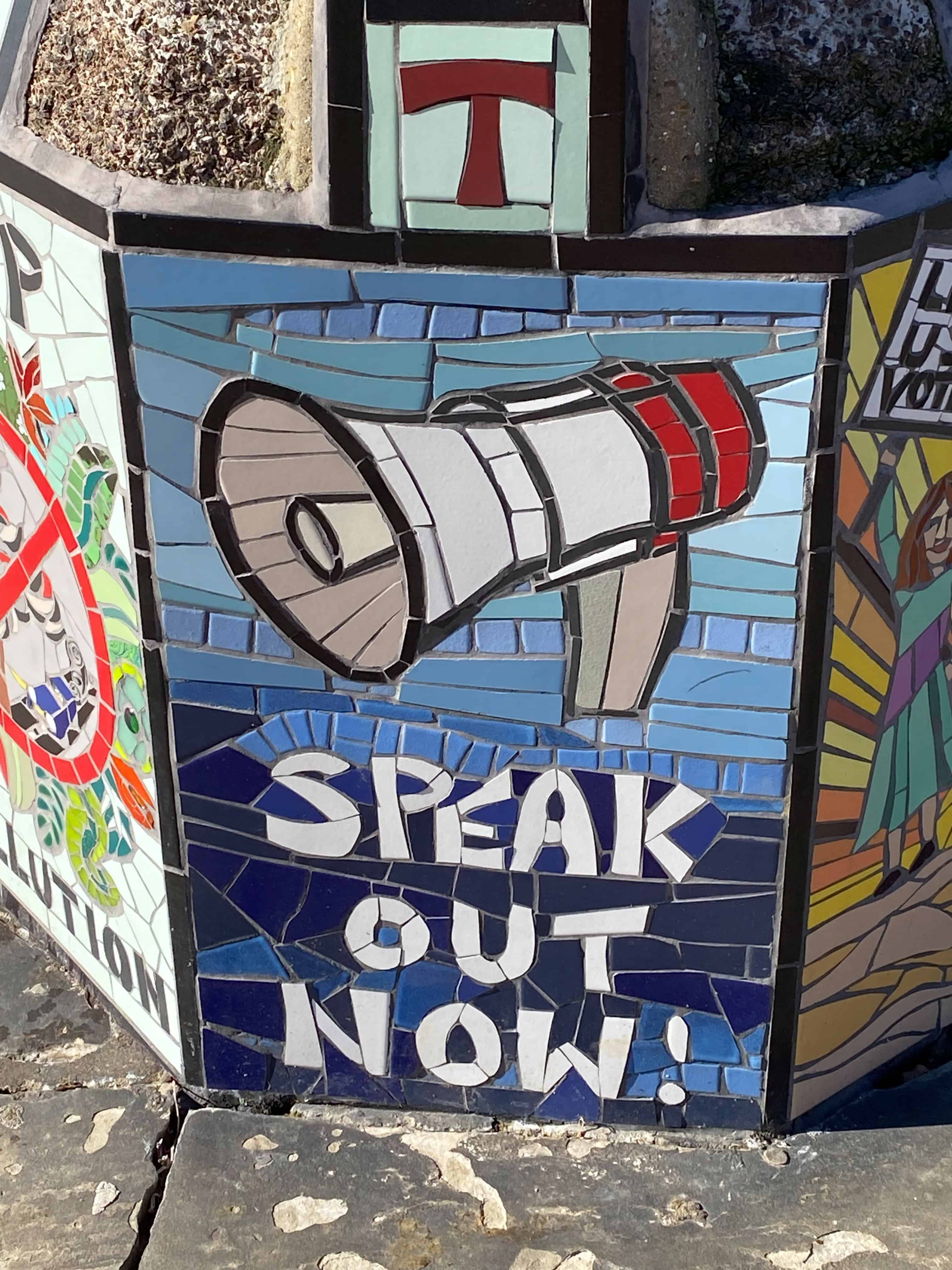 stone mural with speak out now written on it