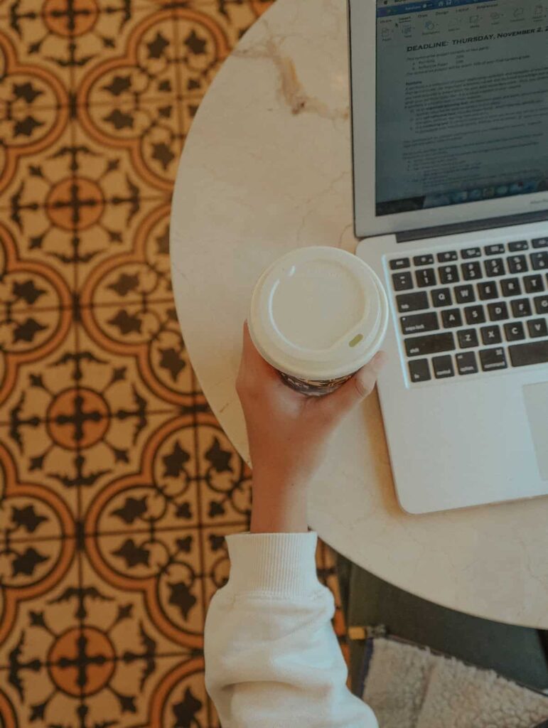 person's hand holding coffee with laptop on table