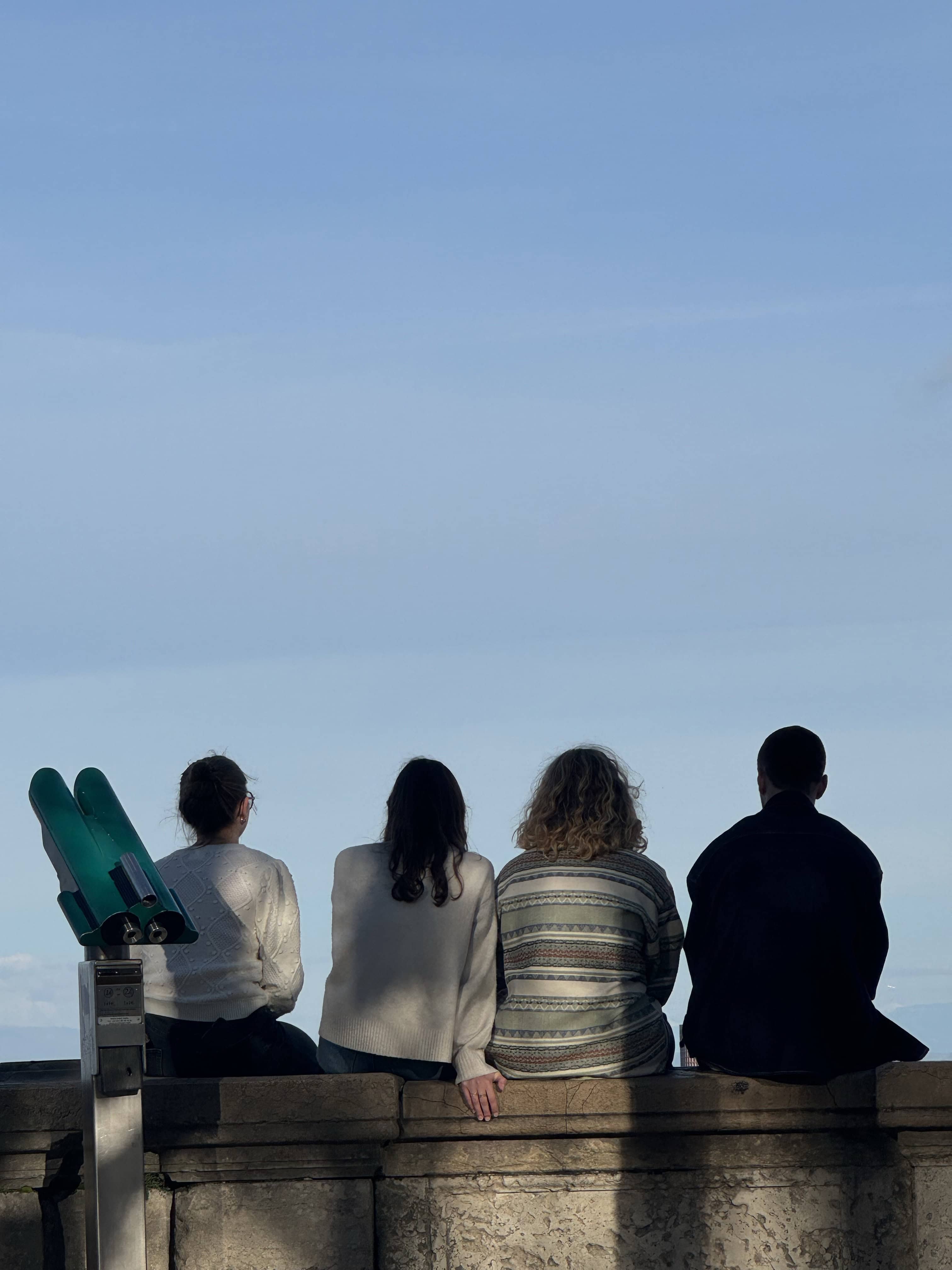 four people sitting on ledge looking into distance