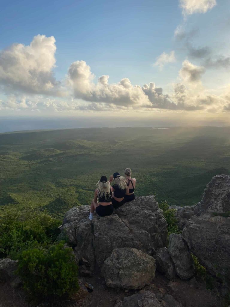 Three women sitting on edge of cliff overlooking forest